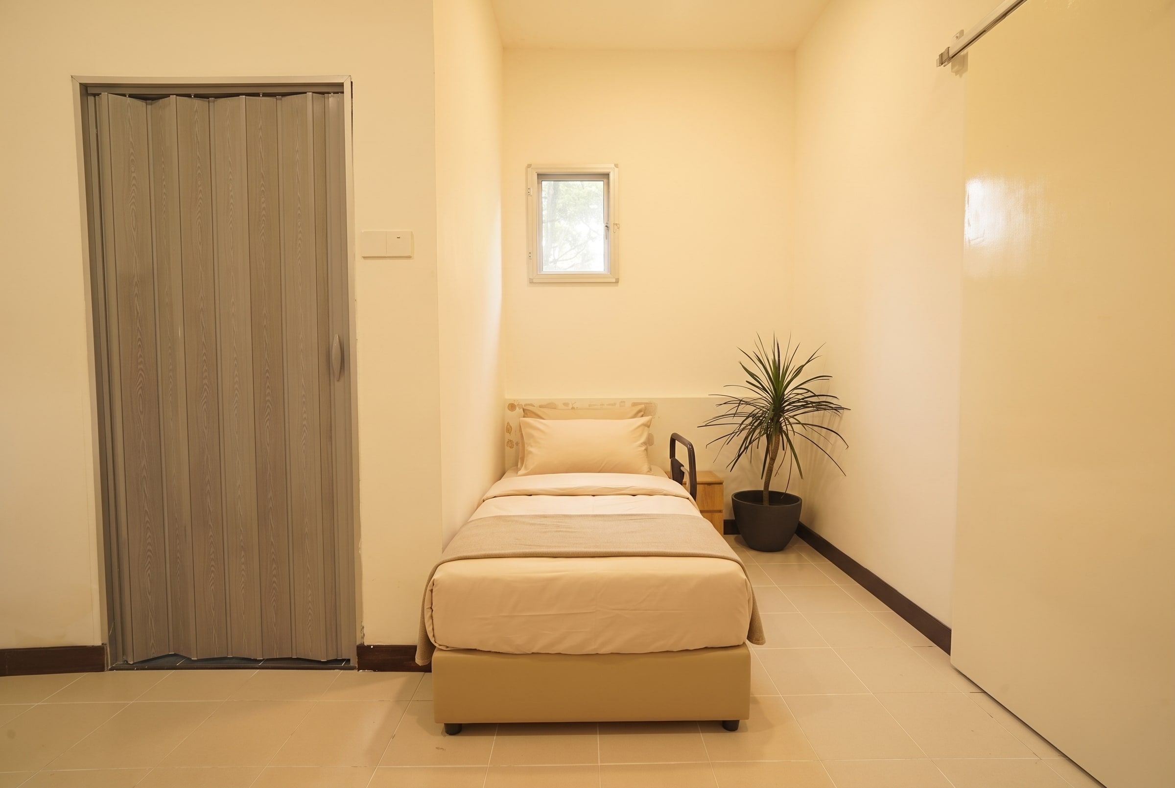 Made-up resident bed beside a folding privacy door and greenery